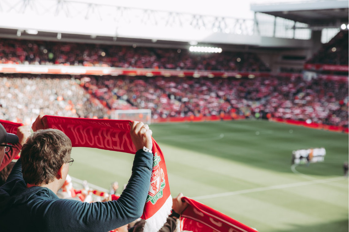 View of Liverpool fans holding red scarves at Anfield Stadium during a football match.