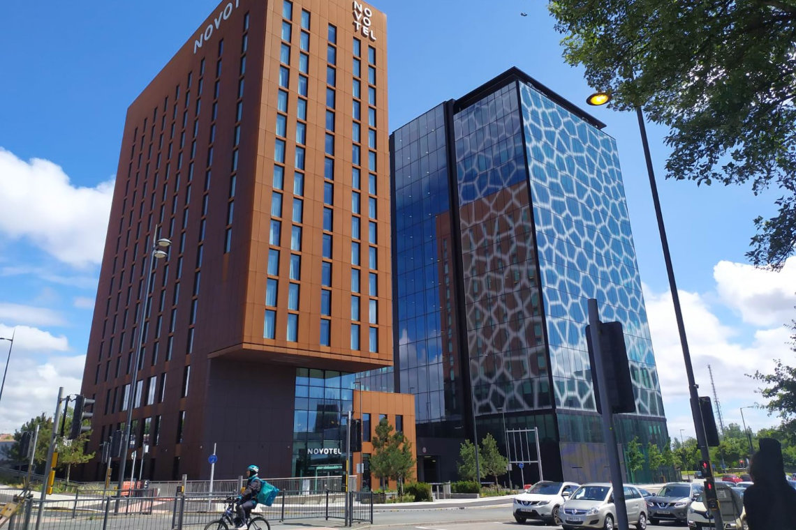 iew of Novotel Liverpool Paddington Village hotel and modern glass building beside main road.